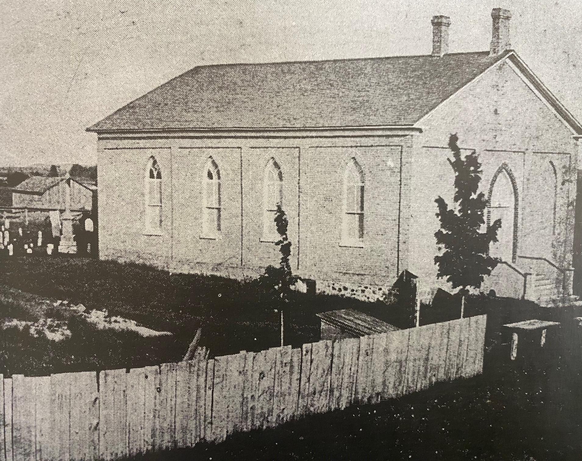 Old photo of the Ratho Presbyterian Church, a small brick building with a cemetery located behind it.