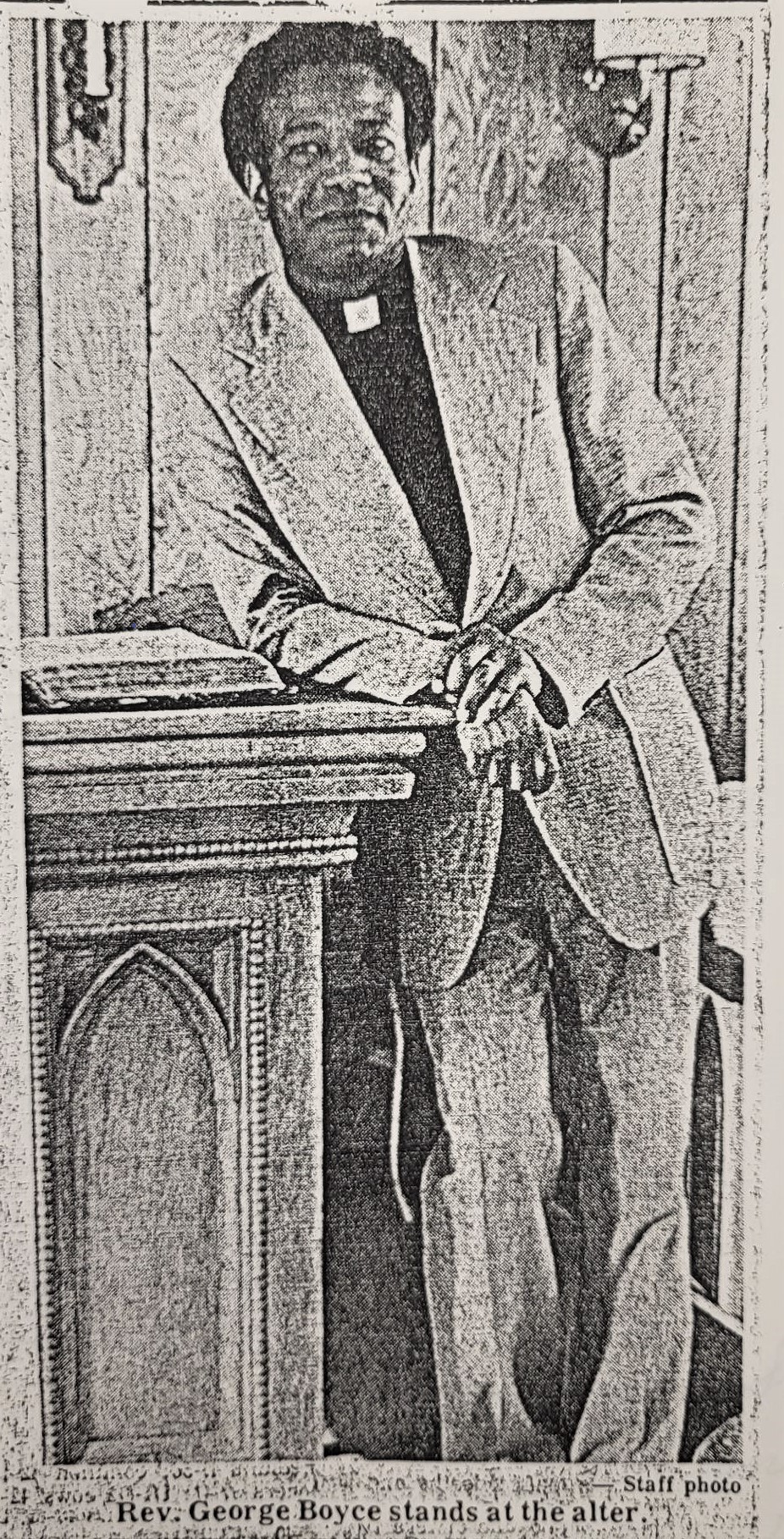 A newspaper photograph of Rev. George Boyce posing in the Park Row Community Chapel. He is leaning on the altar in the church.