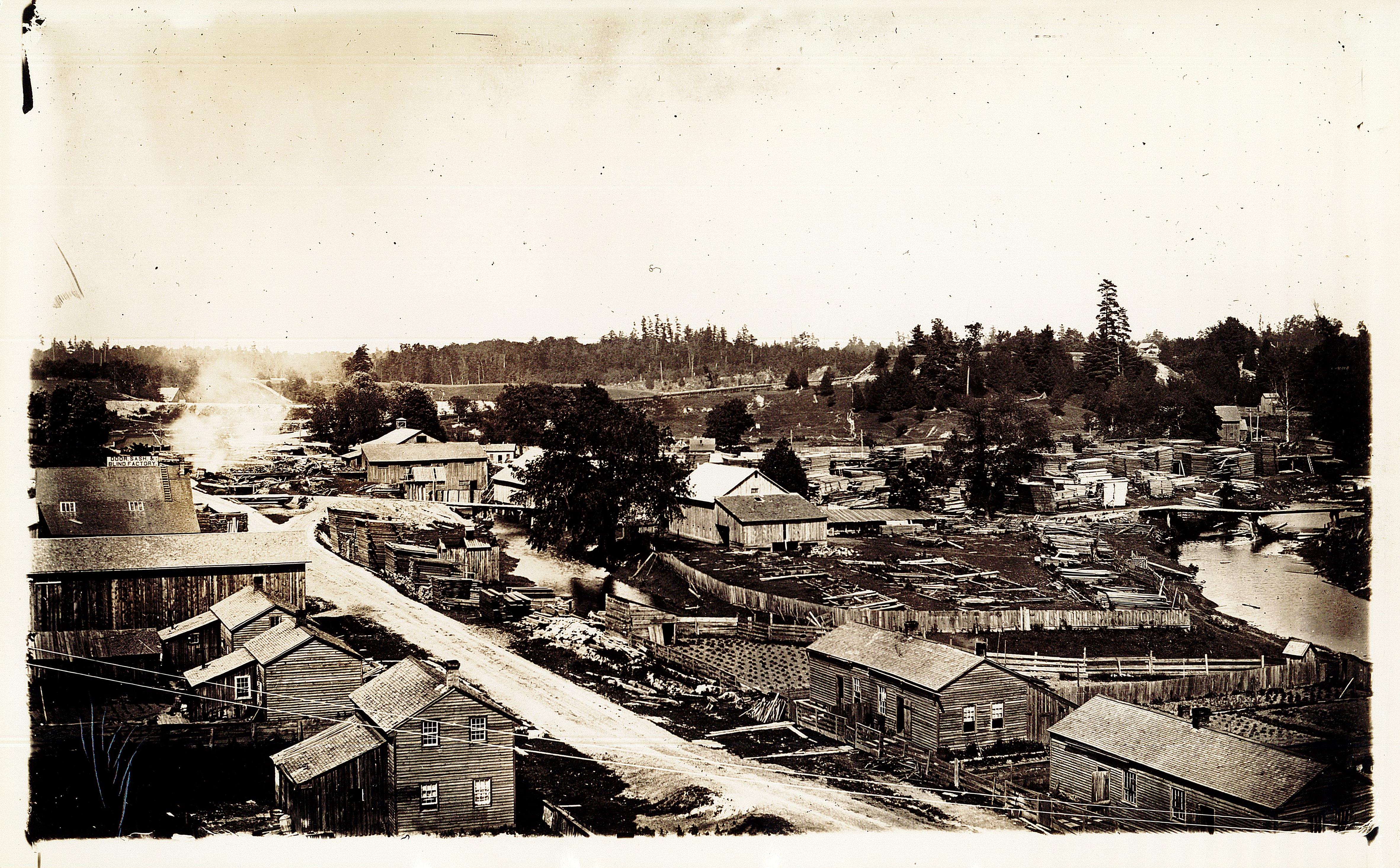 Aerial view of E.D. Tillson's mills and business property. A dirt road runs through a large number of wood frame buildings, a creek runs along the right side of the landscape.