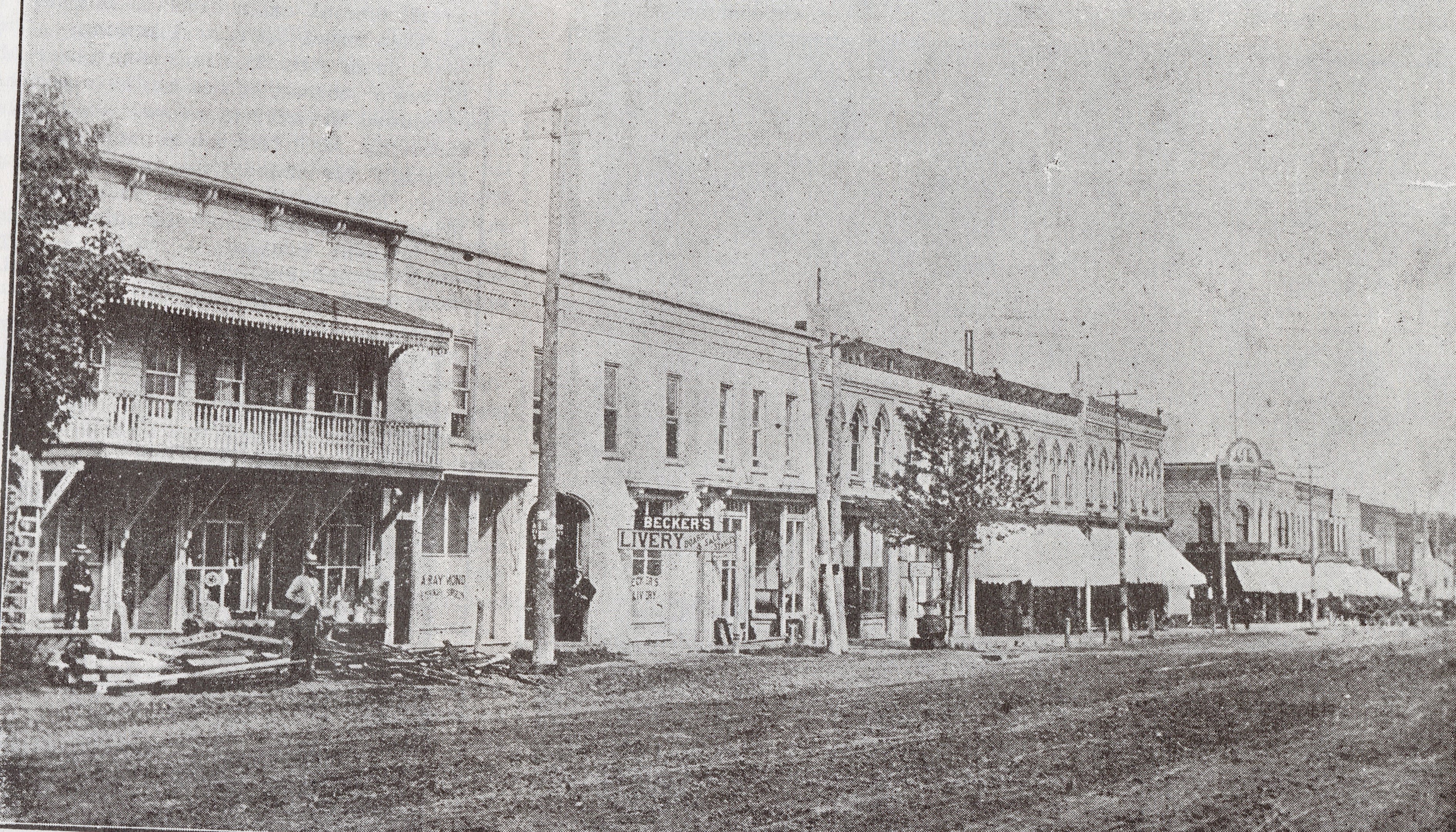 Broadway Street in Tillsonburg, east side looking south. The street is dirt with various building with awnings running along it.